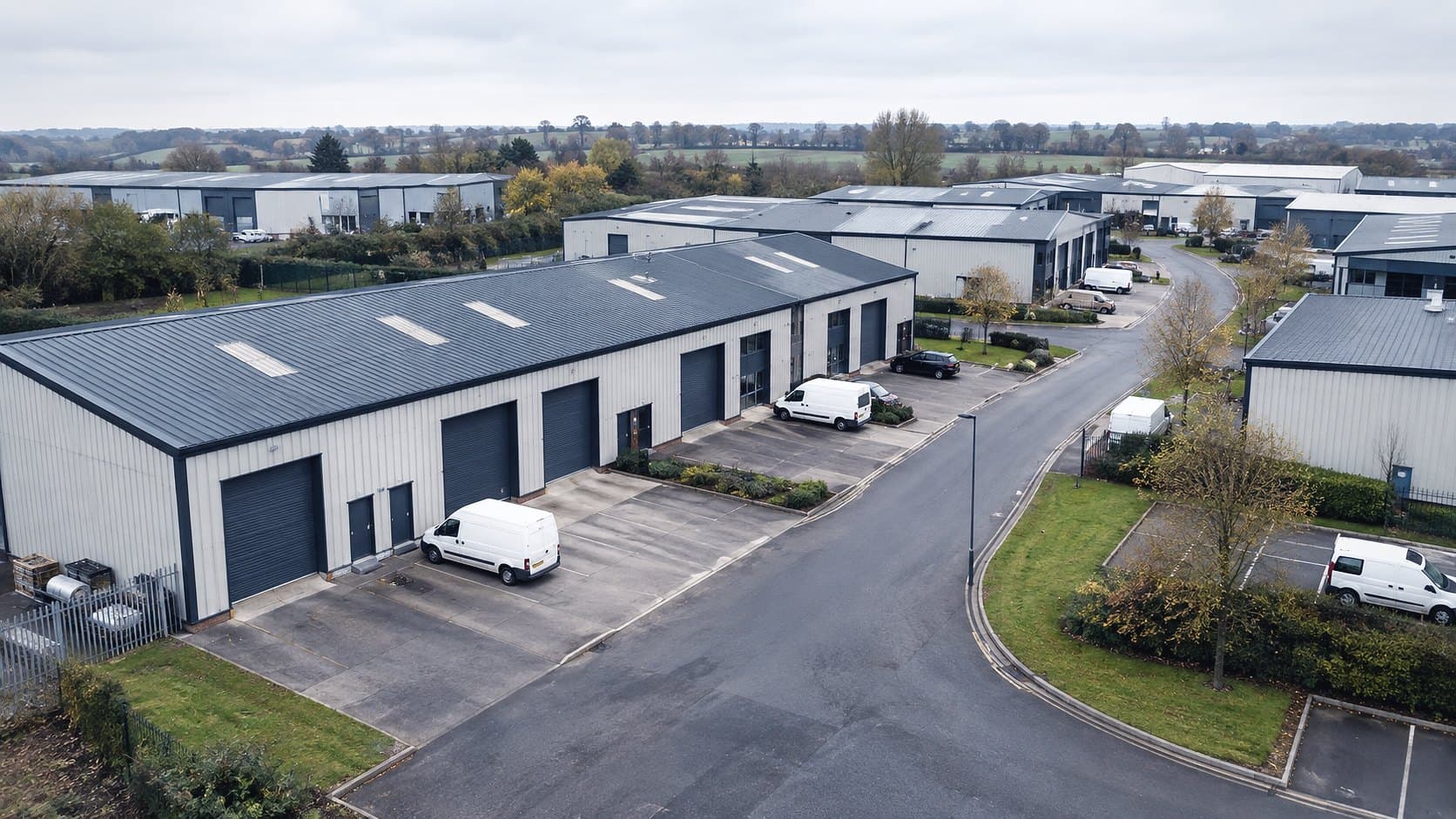 An industrial estate from above: steel clad units with roller doors, vans and a road running through