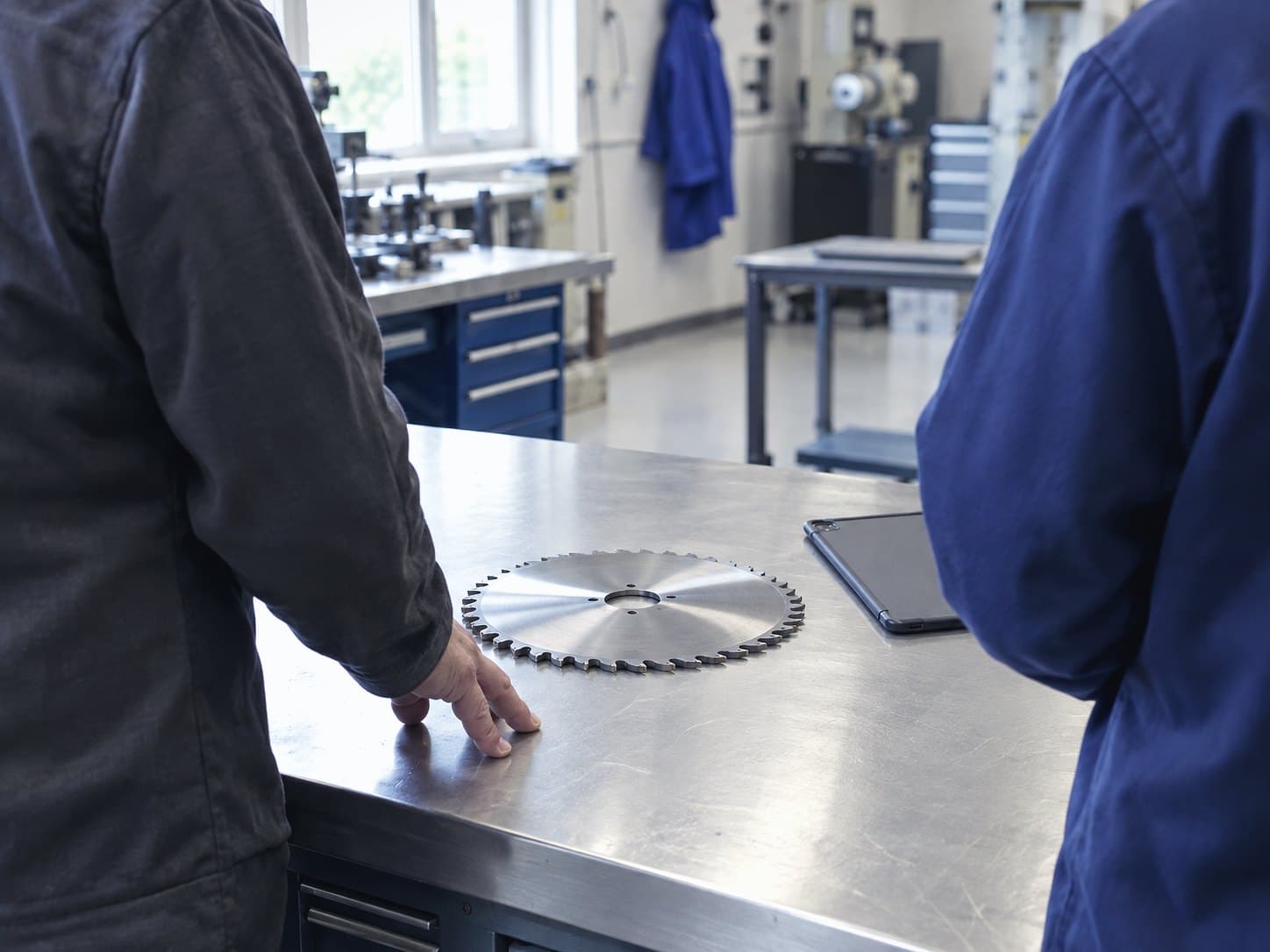 Two people at a workshop bench looking at a reconditioned circular saw blade